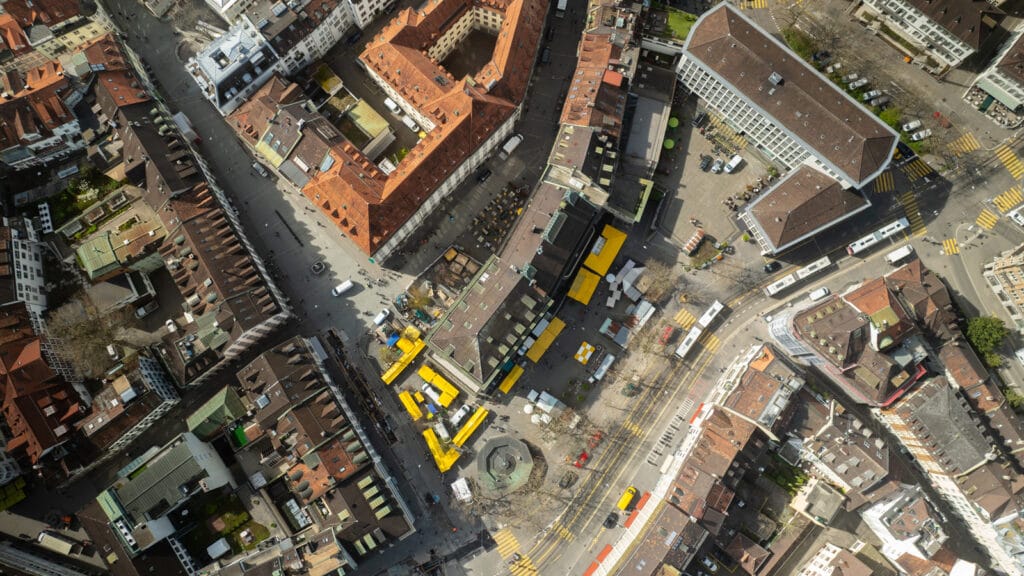 Luftaufnahme des Marktplatzes St. Gallen mit bunten Marktständen und Besucherinnen zwischen den Gassen der Altstadt