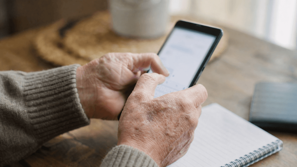 Older hands typing a message on a smartphone next to a notepad